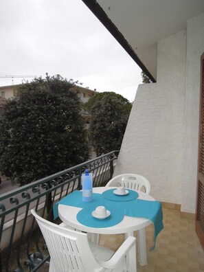 A small balcony with a table and chairs, a water bottle, and a white wall.