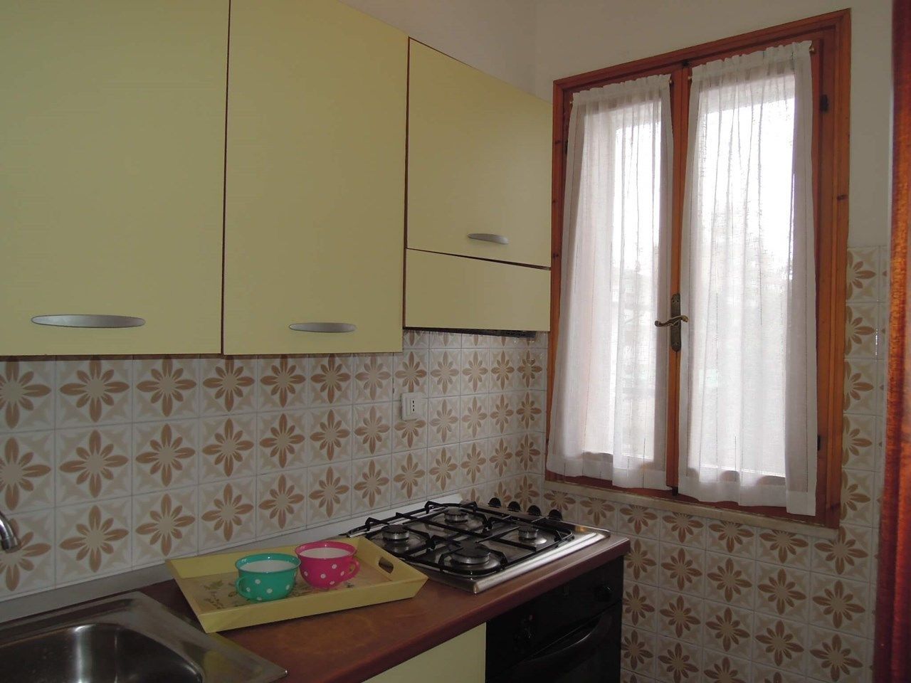 A kitchen with yellow cabinets, a gas stove, and a window with curtains.