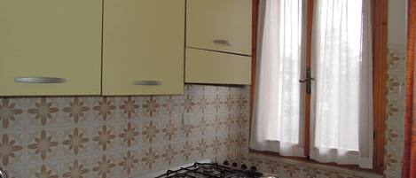A kitchen with yellow cabinets, a gas stove, and a window with curtains.