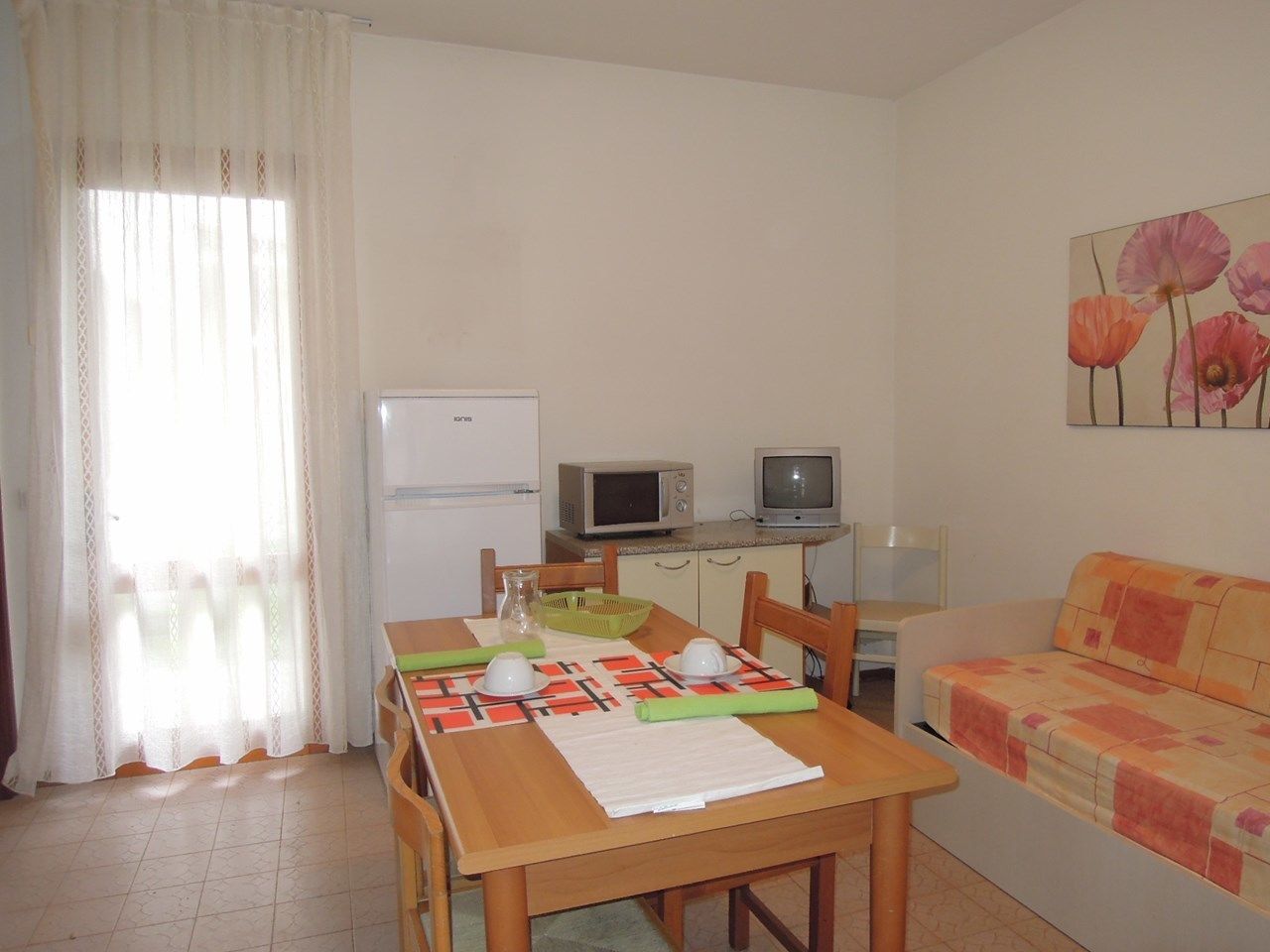 Un espacio habitable compacto con una mesa de comedor, sillas, un sofá, un microondas, un televisor y un refrigerador.