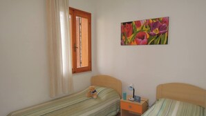 Een slaapkamer met twee enkele bedden, een raam met gordijnen, een nachtkastje met een lamp en een schilderij aan de muur.
