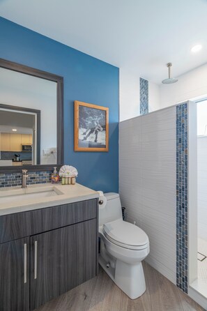 Un baño moderno con una pared azul de acento, un espejo grande, un inodoro y una zona de ducha.