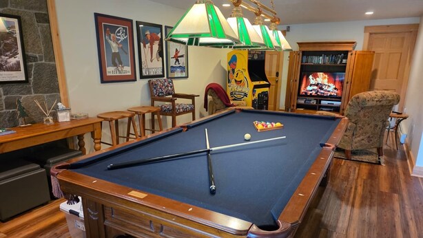A pool table with a cue stick, a billiards ball, and a small trash bin.