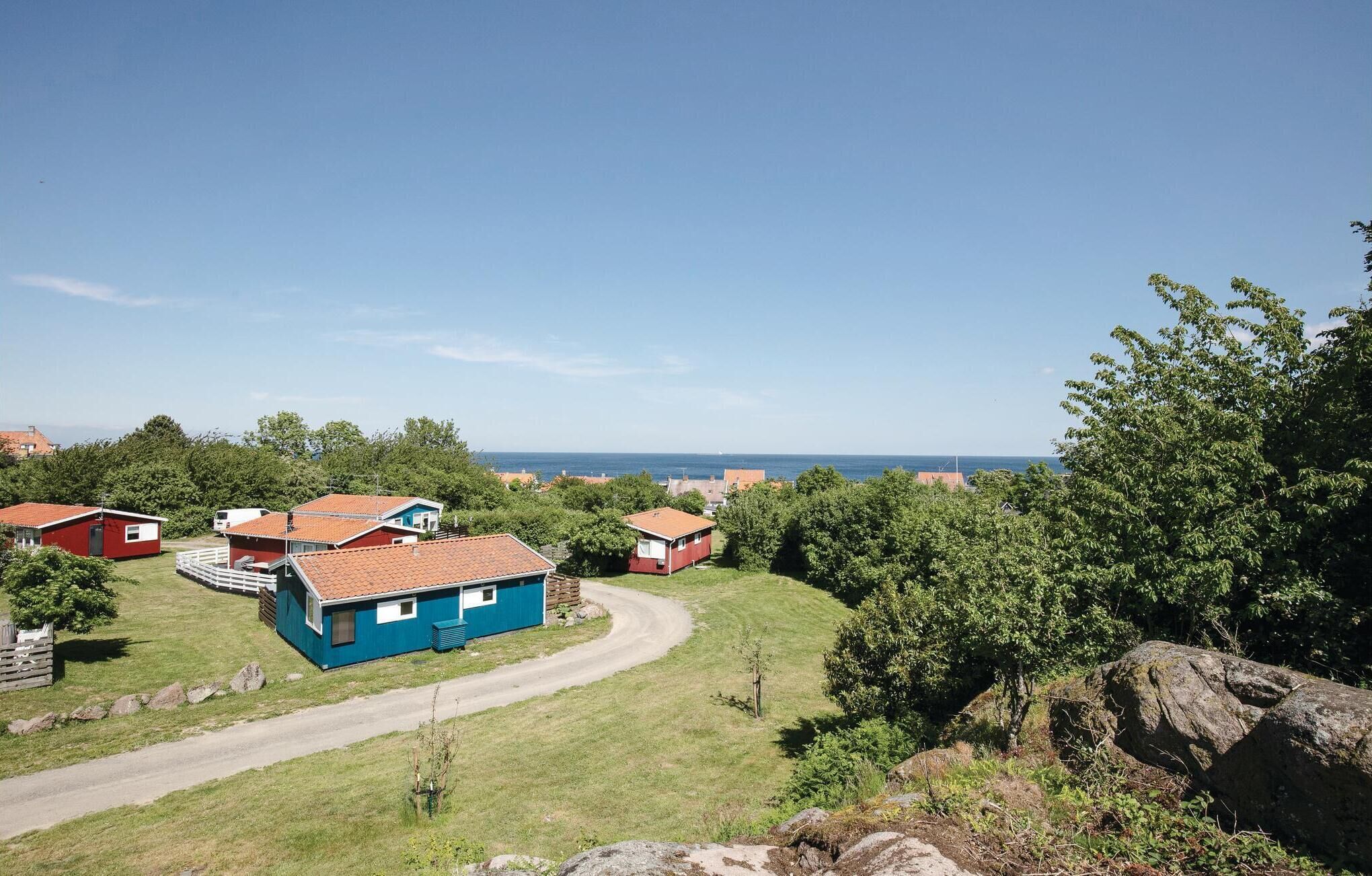 Uma vila costeira com várias casas de telhado vermelho e uma casa azul destacada, com varanda branca.