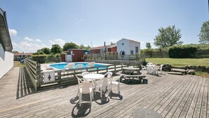 Een houten terras met een zwembad, buitenmeubels en een klein gebouw.