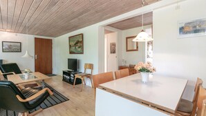 Een moderne woonkamer met een houten plafond, een eethoek met een witte tafel en stoelen, een televisie en kunstwerken aan de muren.