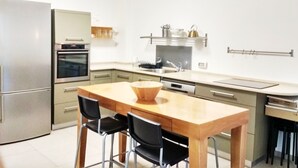 Uma cozinha moderna com uma mesa e cadeiras de madeira, forno embutido e uma geladeira de aço inoxidável.