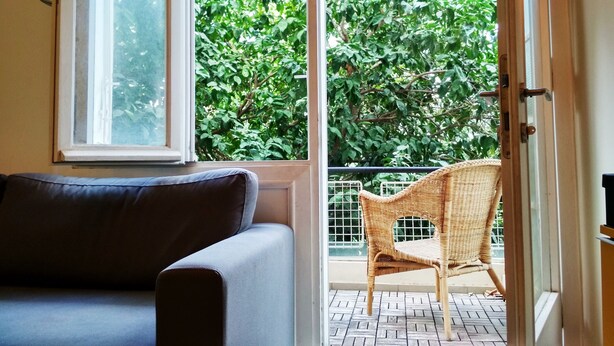 Quarto com sofá, cadeira de vime e vista para um jardim verde através de uma porta de vidro.