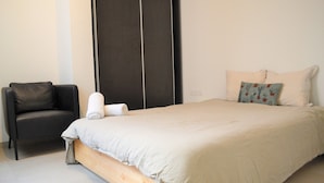 Quarto com cama, uma cadeira e um painel escuro grande.