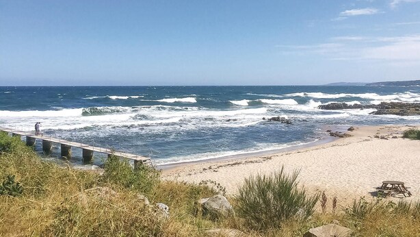 A beach with waves crashing onto the shore, a wooden pier, and a sandy beach with some vegetation in the foreground. - Lovely apartment in Allinge (Allinge)