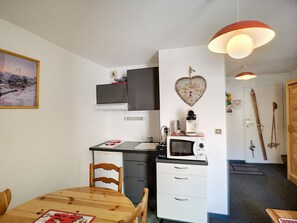 A compact kitchen with a microwave, stove, and cabinets, a dining table with chairs, and a heart-shaped wall decoration.