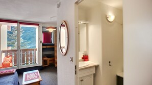 Une petite pièce avec un lit superposé, une petite table avec un set de table rouge, un lavabo blanc et un miroir.