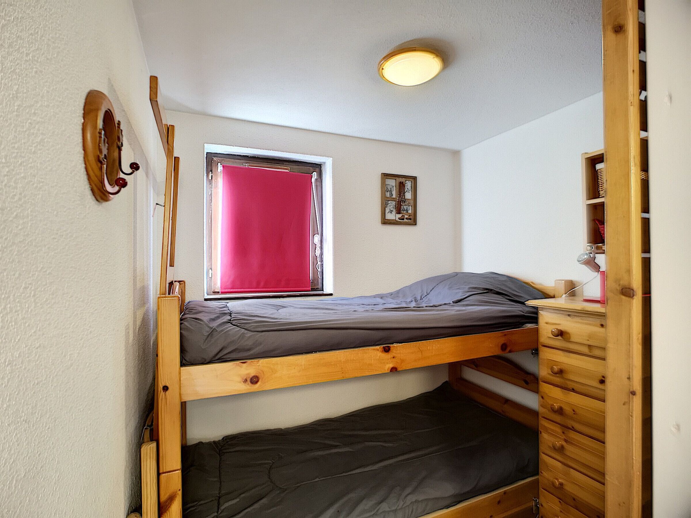 A bunk bed room with a window, a small desk, and a wooden dresser.