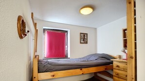 Une chambre avec un lit superposé, une fenêtre, un petit bureau et une commode en bois.