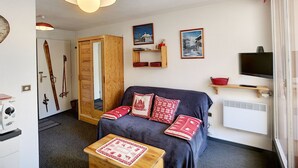 Une pièce chaleureuse avec un canapé bleu foncé, des coussins à motifs rouges et blancs, une table basse en bois et un téléviseur posé sur une étagère.