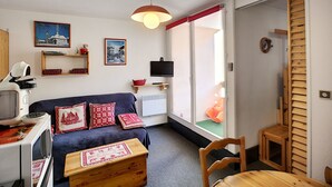 Un espace de vie compact comprenant un canapé, une petite table, un téléviseur et un meuble en bois.