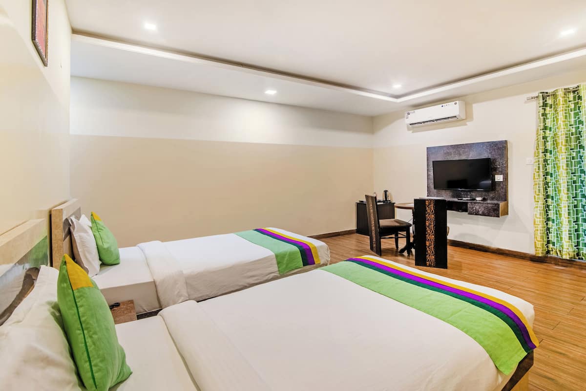 A hotel room with two beds, a desk, a TV, and an air conditioning unit.