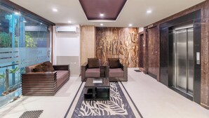 A hotel lobby with a modern design, featuring a sofa set, a coffee table, a decorative wall, and an elevator. - Treebo Address Inn, Banjara Hills (Hyderabad)