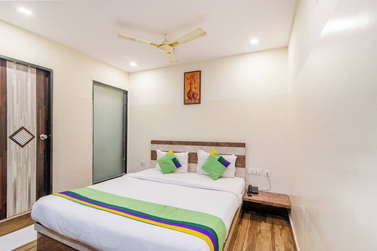 A hotel room with a bed, a nightstand, a ceiling fan, a door, and a wall-mounted artwork.
