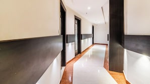 A modern hotel corridor with dark and light walls, a marble floor, and doors with decorative panels. - Treebo Address Inn, Banjara Hills (Hyderabad)