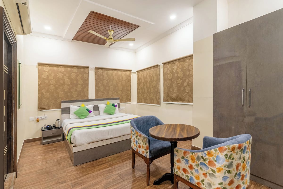 A hotel room with a bed, a chair, a small table, a wardrobe, and a ceiling fan.