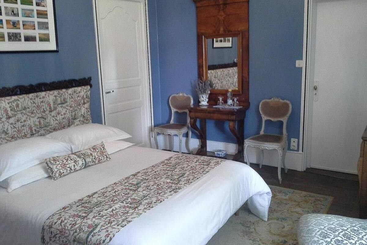 A bedroom with a bed, two chairs, a dresser, and a mirror.