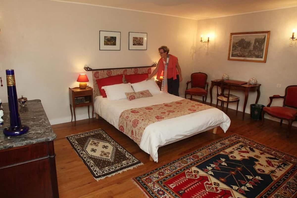 A bedroom with a bed, nightstands, a desk, and chairs.