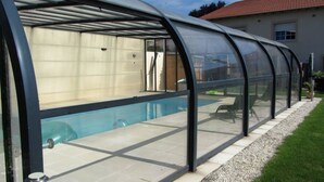 Una piscina exterior cubierta con techo transparente, rodeada por un patio empedrado y un borde de grava.