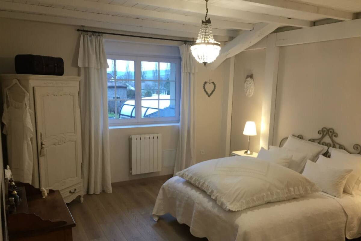 Une chambre à coucher comprenant un lit, une commode, une fenêtre avec des rideaux, un radiateur et un lustre.