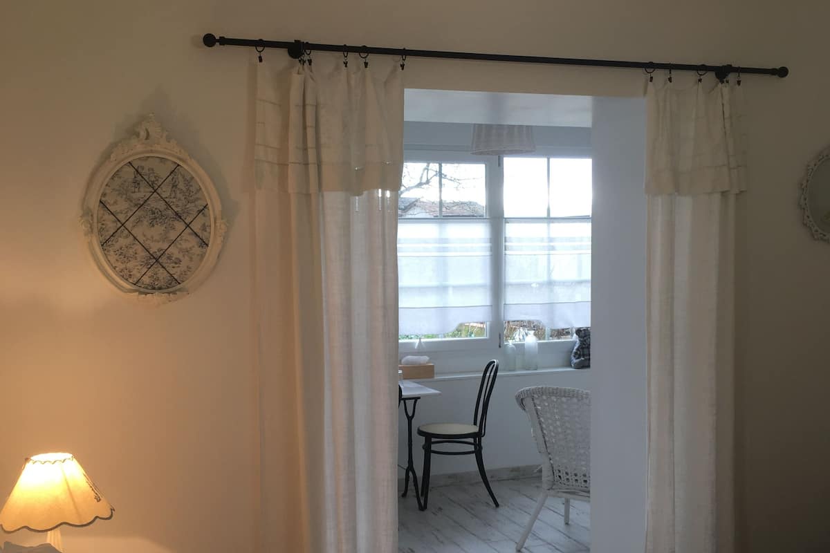 Une chambre à coucher comprenant un lit, une table et une chaise, dans une pièce lumineuse donnant sur l’extérieur.