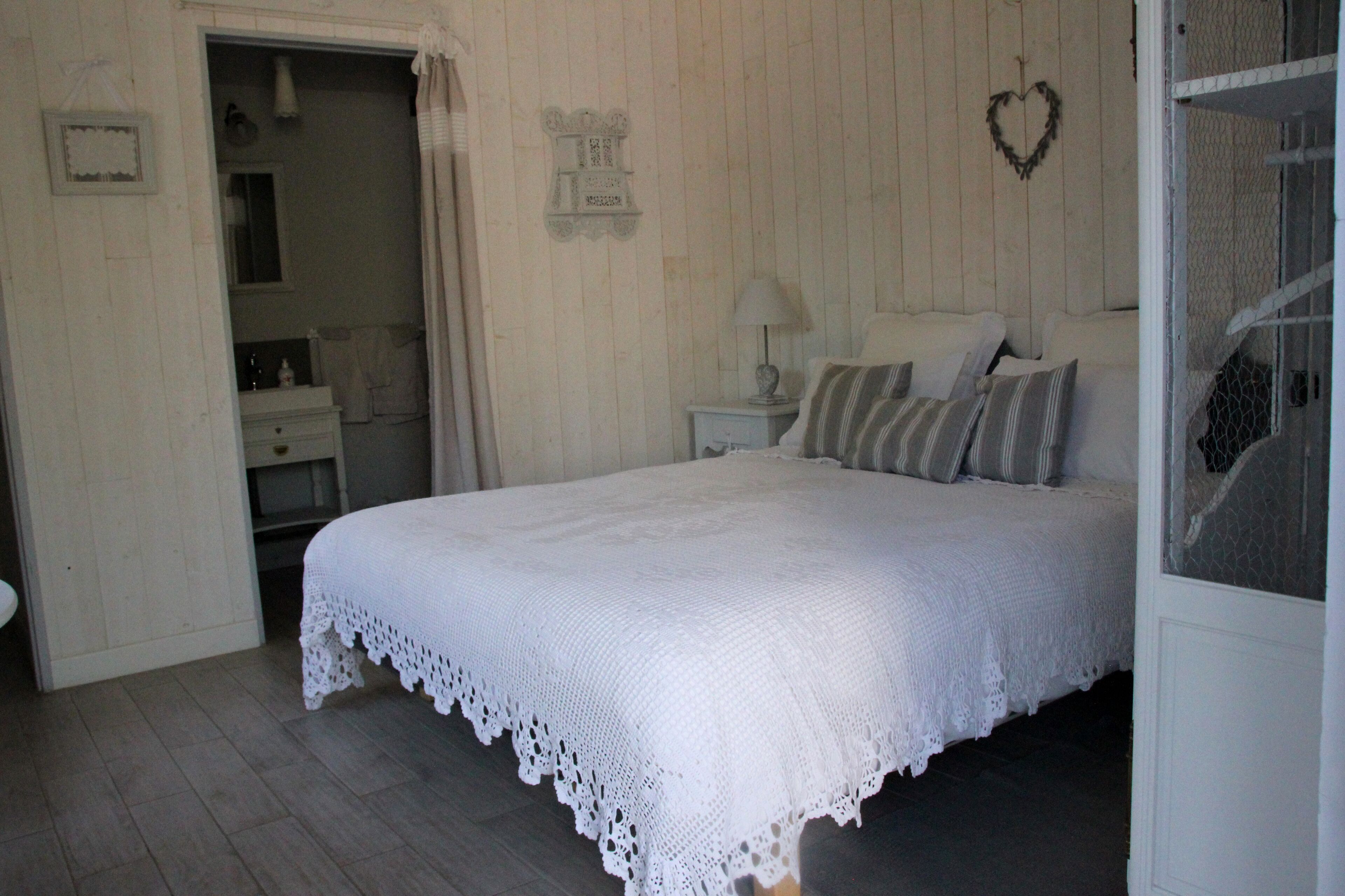 A bedroom with a white bed, a nightstand with a lamp, and a mirror.