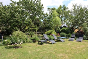 Een tuin met vier loungestoelen, een kleine tafel en een prieel.