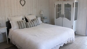Un dormitorio con una cama grande, paredes blancas, un armario de madera y una decoración con forma de corazón en la pared.