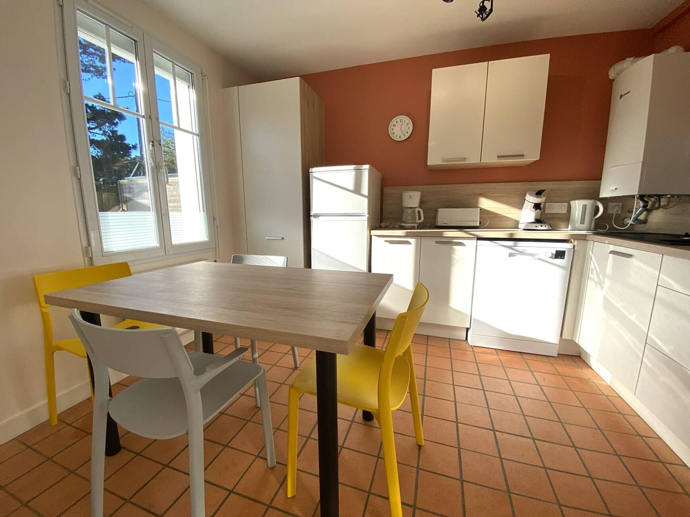 A compact kitchen with white cabinets, a dining table with two chairs, and a window with blinds.