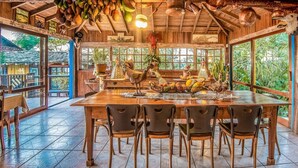 A rustic dining area with a wooden table, chairs, and a view of lush greenery outside. - Pousada Casa do Ceo (Imbituba)