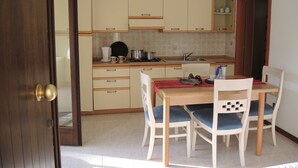 Una cocina con armarios color crema, una mesa de madera con sillas y un mantel rojo.