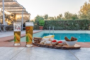 Two glasses of beer and a tray with various snacks by a poolside.