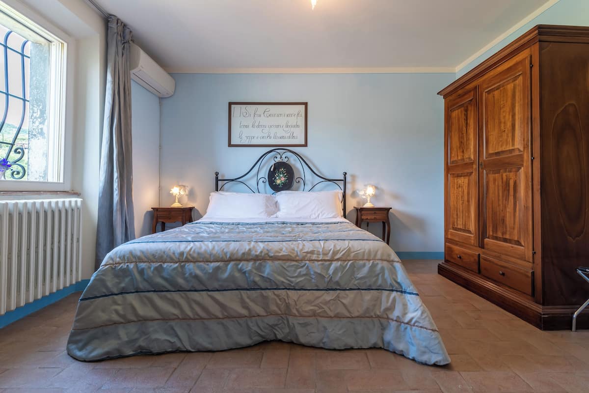 A bedroom with a bed, a wooden wardrobe, a radiator, and a window with curtains.