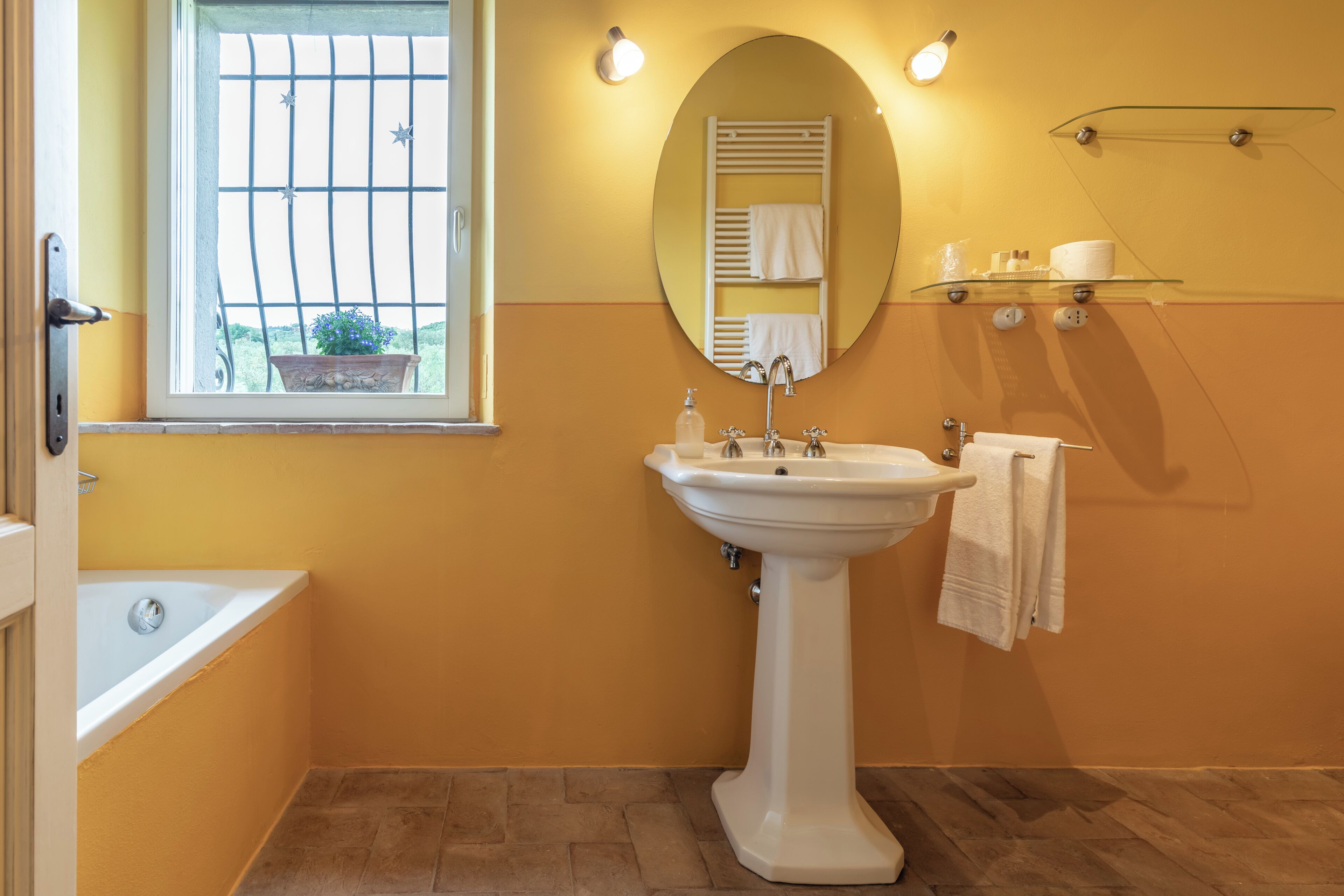 Une salle de bain avec une baignoire, un lavabo, un miroir et une fenêtre donnant sur l’extérieur.