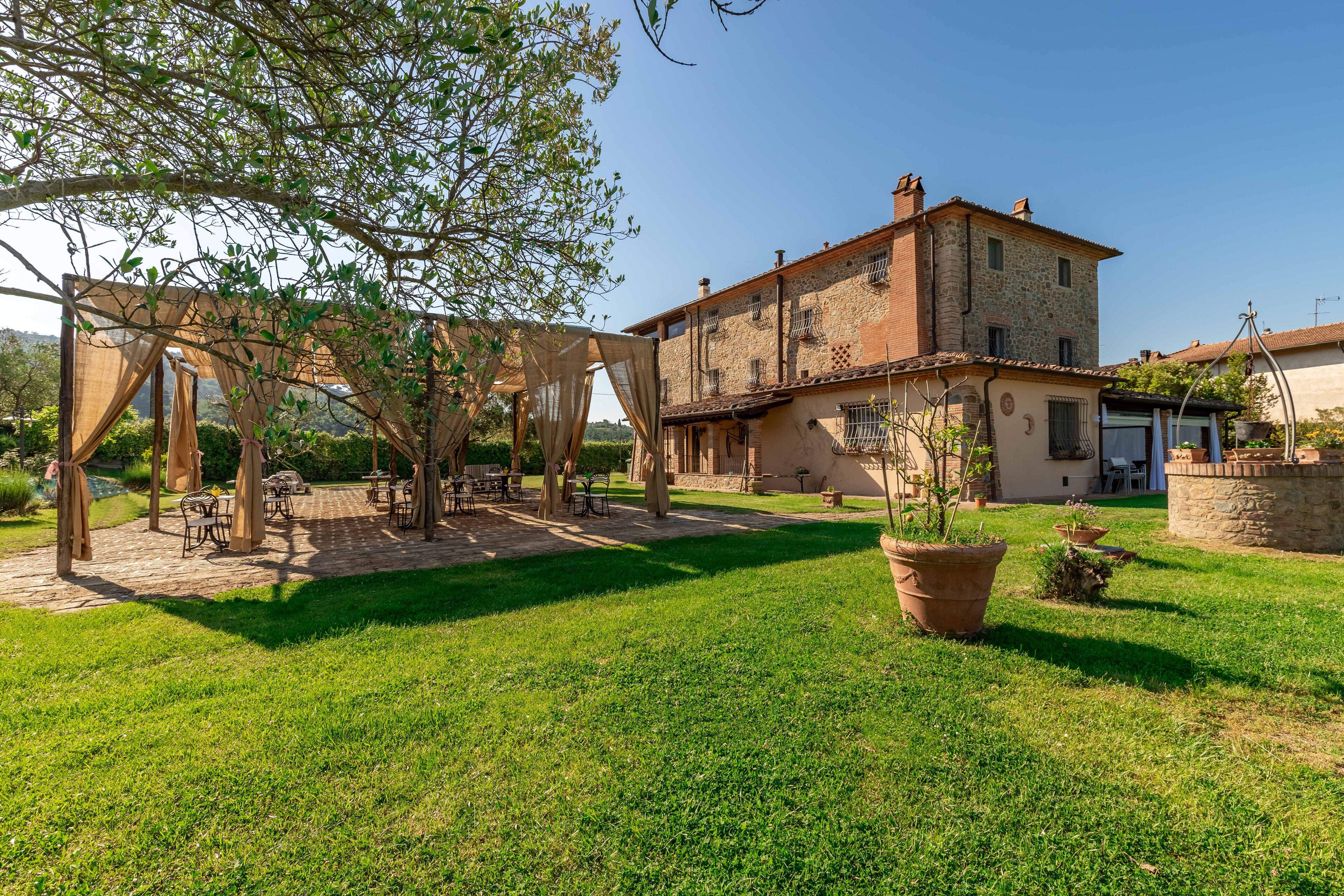 Un cortile con una pergola, posti a sedere all'aperto e un edificio in pietra con numerose finestre e balconi.
