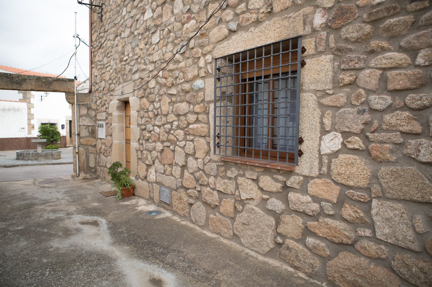 Un edificio de piedra con una ventana de barrotes, una puerta pequeña y una planta en maceta.