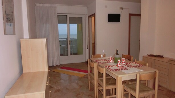 Una habitación pequeña y bien iluminada con una mesa de comedor preparada para cuatro personas, un aparador de madera y un ventanal corredero que da a un balcón.
