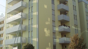 Un edificio de varios pisos con balcones, una ventana visible y una cerca.