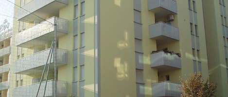 A multi-story building with balconies, a visible window, and a fence.