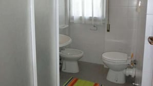 Un baño con dos inodoros, un lavamanos y una ventana con cortinas.