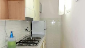 Cocina compacta con estufa a gas, lavamanos y armarios de madera.