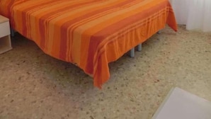 Habitación de hotel con una cama individual, una mesita de noche, una lámpara y una ventana con cortinas.