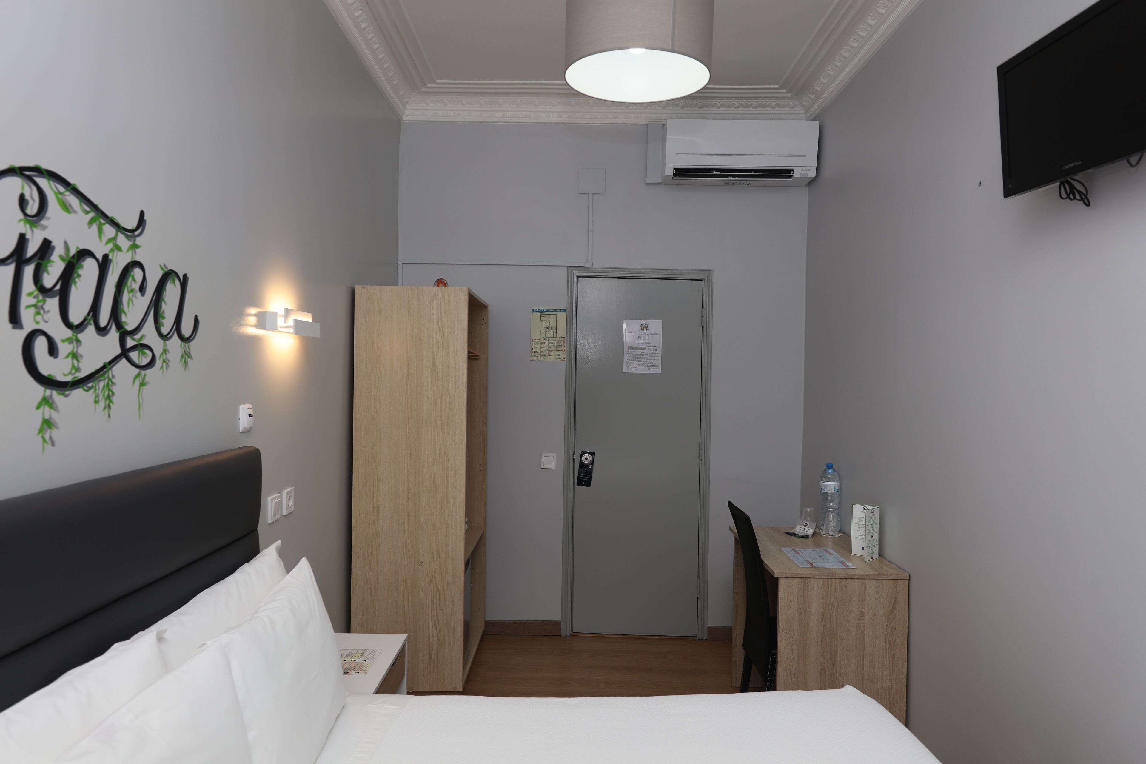 Habitación de hotel con cama, escritorio, armario, equipo de aire acondicionado y televisor montado en la pared.