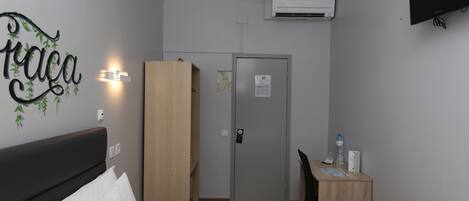 Habitación de hotel con cama, escritorio, armario, equipo de aire acondicionado y televisor montado en la pared.