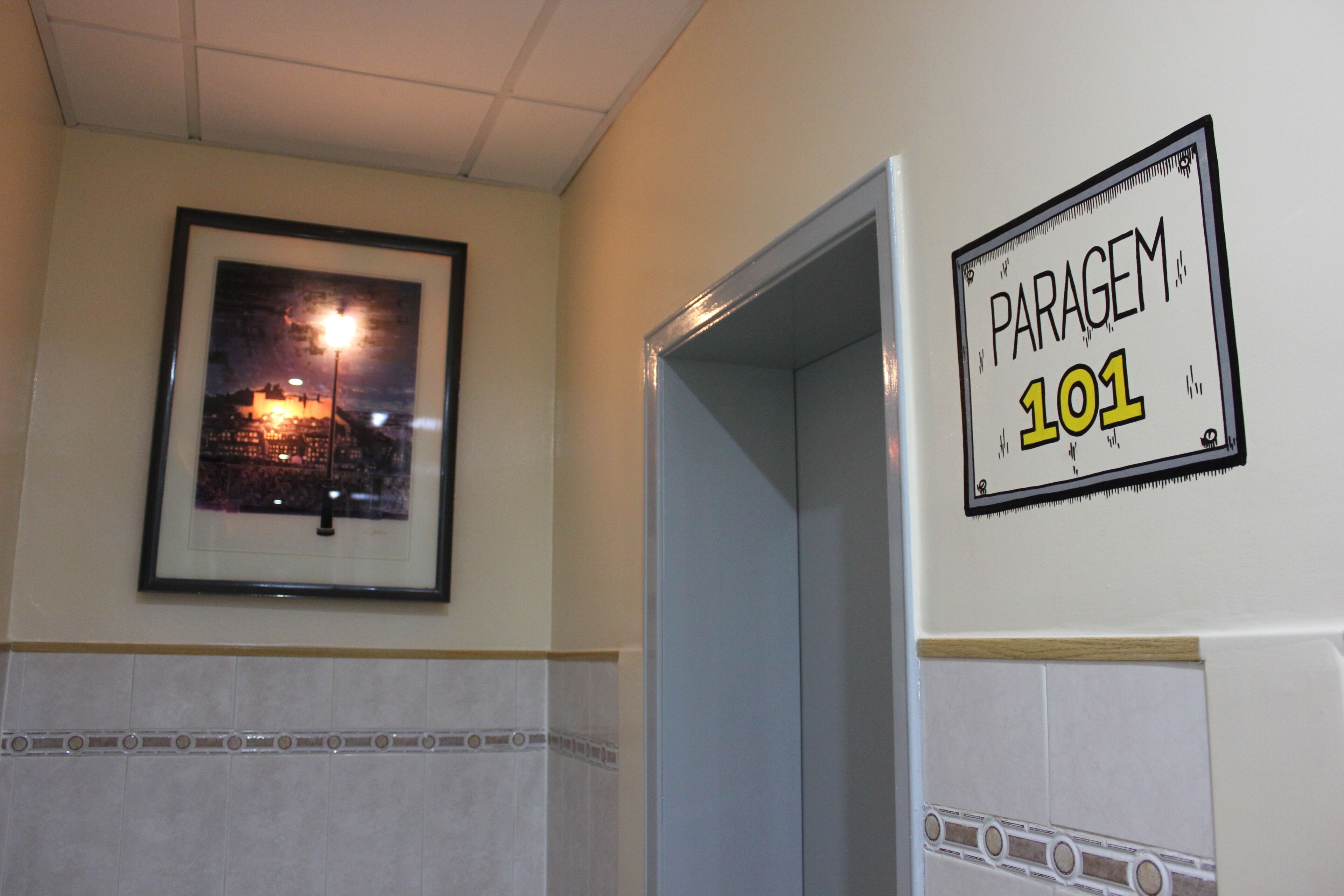 A framed picture of a cityscape on the wall, a sign reading "PARAGEM 101", and a tiled wall with a decorative border.